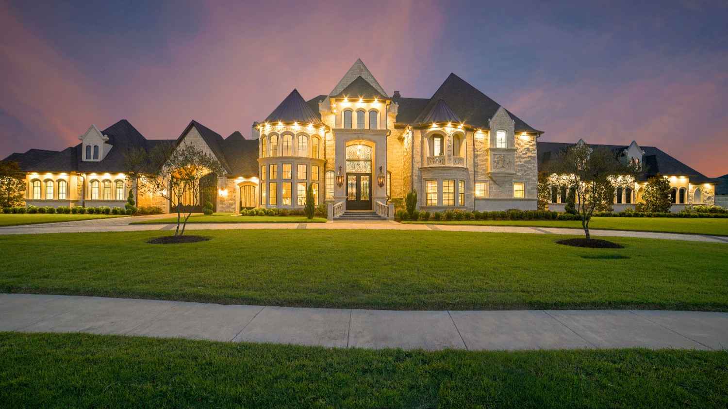 Illuminated stone manor at dusk behind a broad lawn